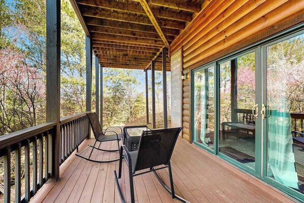 A wooden deck with a glass door, two rocking chairs, and a table. - Lost Indian Hideaway (Whittier)