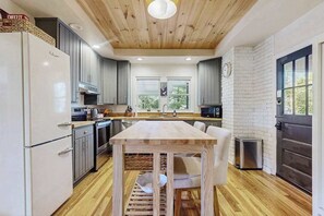 A modern kitchen with wooden ceiling, white brick walls, and a large window. - Huckleberry Hill (Waynesville)