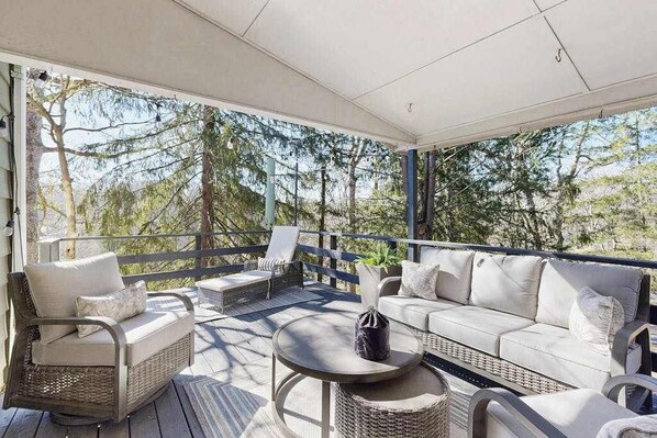 A covered outdoor seating area with wicker furniture and a round table, overlooking a natural landscape. - Huckleberry Hill (Waynesville)
