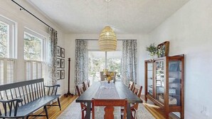 Un comedor con una mesa larga, sillas, un banco, una lámpara colgante y un aparador con puertas de cristal.