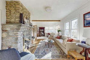 A living room with a stone fireplace, a sofa, a coffee table, and a large window. - Huckleberry Hill (Waynesville)