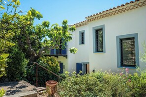 A white building with blue trim and a tiled roof, surrounded by greenery and a large tree. - Villa in Carqueiranne, 5 bedrooms, 5 bathrooms, heated pool, air conditioning. Beach 2.5km away (Carqueiranne)