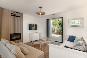 A modern living room with a sofa, a coffee table, a TV, a fireplace, a sliding glass door leading to an outdoor area, and a bed with pillows. - Villa in Carqueiranne, 5 bedrooms, 5 bathrooms, heated pool, air conditioning. Beach 2.5km away (Carqueiranne)