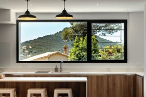 Una cocina con un ventanal grande, armarios de madera, un lavabo y dos lámparas colgantes.