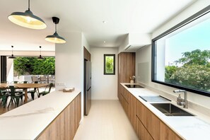 Una cocina moderna con un ventanal amplio, armarios de madera e iluminación colgante.