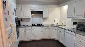 A kitchen with white cabinets, a dark wood floor, a stainless steel sink, and a built-in oven. - Appomattox Family House (College Station)