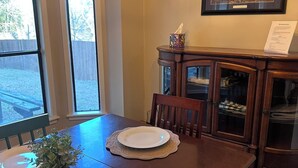 A dining room with a wooden table set for two, a chandelier, a framed painting, and a cabinet with glass doors. - Appomattox Family House (College Station)