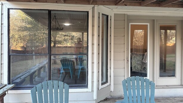 A covered porch with a wooden ceiling, large windows, and two blue chairs. - Appomattox Family House (College Station)