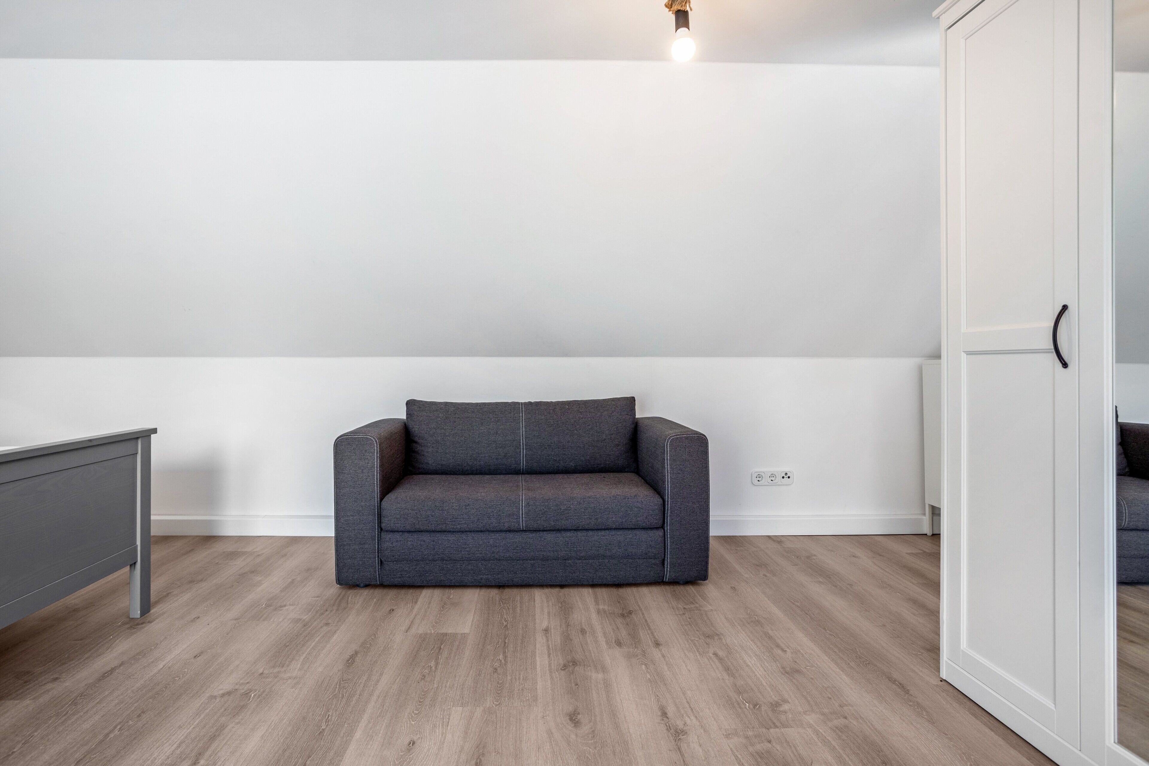 Een kamer met een grijze bank, een grijze kast en een witte inbouwkast.