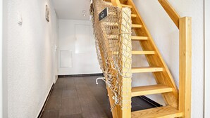 Eine Holztreppe mit einem Netz als Geländer, eine weiße Tür und eine strukturierte Wand.