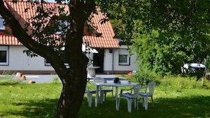 A table with chairs outside a building with a red-tiled roof, surrounded by greenery.