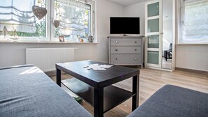 Ein modernes Wohnzimmer mit einer Couch, einem kleinen Tisch, einem Fernseher und einem Fenster mit Vorhängen.