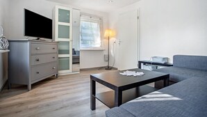 Ein modernes Wohnzimmer mit einer Couch, einem Fernseher, einem Schreibtisch und einer Lampe.