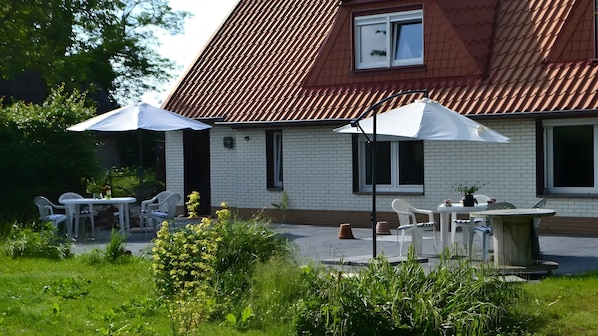 A house with a red roof, white brick exterior, and a patio with outdoor furniture and umbrellas.