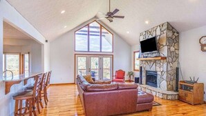 A spacious living room with a stone fireplace, a large window, and a dining area with wooden chairs. - Everview (Waynesville)