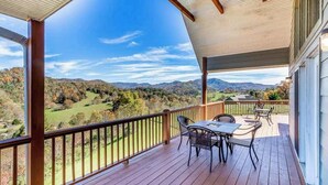A covered outdoor deck with a table and chairs, overlooking a scenic landscape. - Everview (Waynesville)