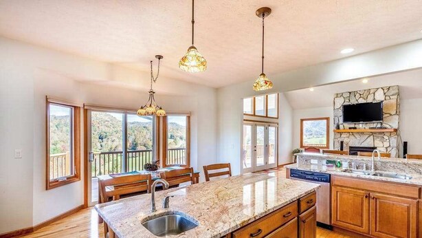 A kitchen with a granite countertop, wooden cabinets, a built-in dishwasher, and a stone backsplash. - Everview (Waynesville)