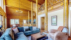 Ein Blockhaus-Interieur mit Ecksofa, Couchtisch, gepolstertem Sessel und Holzbalkendecke.