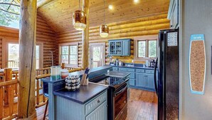 Ein rustikales Blockhaus-Interieur mit einer Küche, die Holzschränke, eine zentrale Kochinsel und hängende Pendelleuchten zeigt.