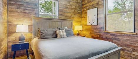 Une chambre avec un mur décoré de panneaux en bois, un lit avec une literie grise, deux lampes de chevet et un tableau encadré accroché au mur.
