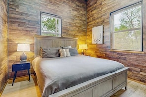 Ein Schlafzimmer mit Wandpaneelen aus Holz, einem Bett mit grauer Bettwäsche, zwei Nachttischlampen und einem gerahmten Bild an der Wand.