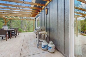 Une terrasse extérieure équipée d’un barbecue, d’une table à manger, de chaises et de bouteilles de propane.