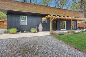 Un bâtiment moderne à l’extérieur sombre, doté d’une pergola en bois et d’une allée gravillonnée.