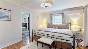 Ein Schlafzimmer mit einem Bett, Nachttischlampen, einer Pendelleuchte, einer Bank und einer Tür zu einem anderen Raum.