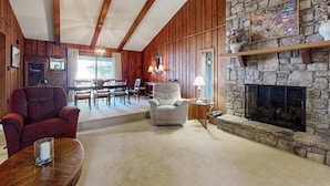 Una sala de estar acogedora con chimenea de piedra, vigas de madera, comedor y un sillón rojo.