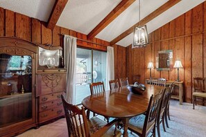 Ein Zimmer mit Holzwänden, einem großen Esstisch aus Holz, Stühlen, einem Schrank und einer Kandelaber.