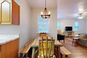 Ein Essbereich mit einem rustikalen Holztisch und Stühlen, einer Chandelierleuchtre und einem Fernseher im Hintergrund.