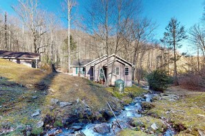 Eine rustikale Holzhütte mit geneigtem Dach, einer kleinen Veranda und einem Bach davor.