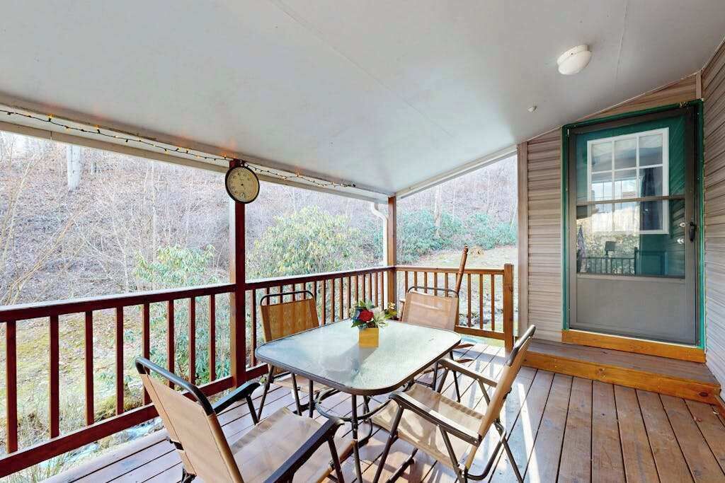 A covered porch with a table and chairs, a clock, and a door with a green frame.