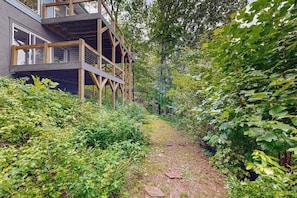 Eine Holzterrasse mit einer Treppe, die zu einem Gebäude führt, umgeben von dichtem Grün.