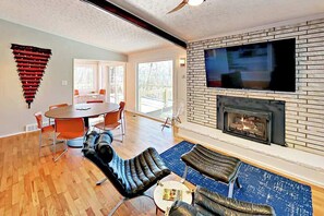 Ein modernes Wohnzimmer mit Kamin, einem an einer Ziegelwand montierten Fernseher und einem Essbereich mit rundem Tisch und Stühlen.