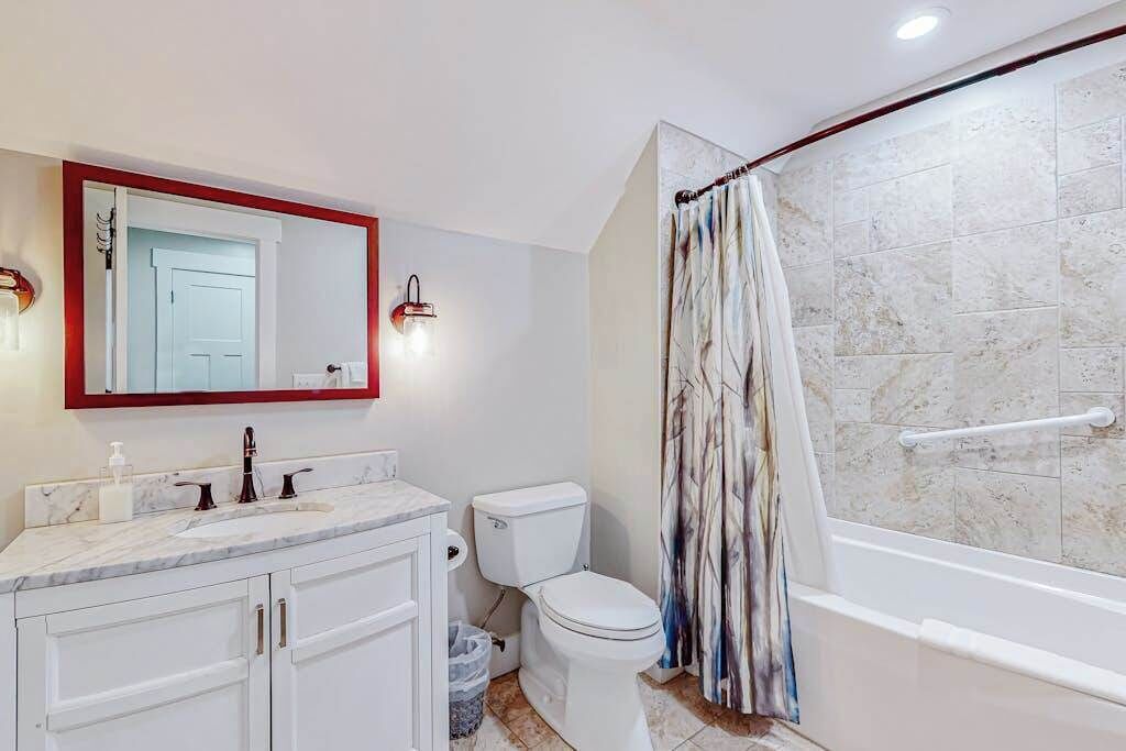Een badkamer met toilet, wastafel, spiegel, douchegordijn en betegelde wanden.