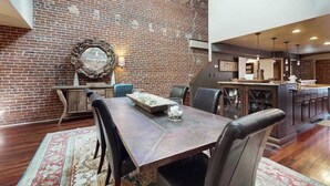 Un comedor con pared de ladrillo, un espejo redondo y una mesa de madera con sillas.