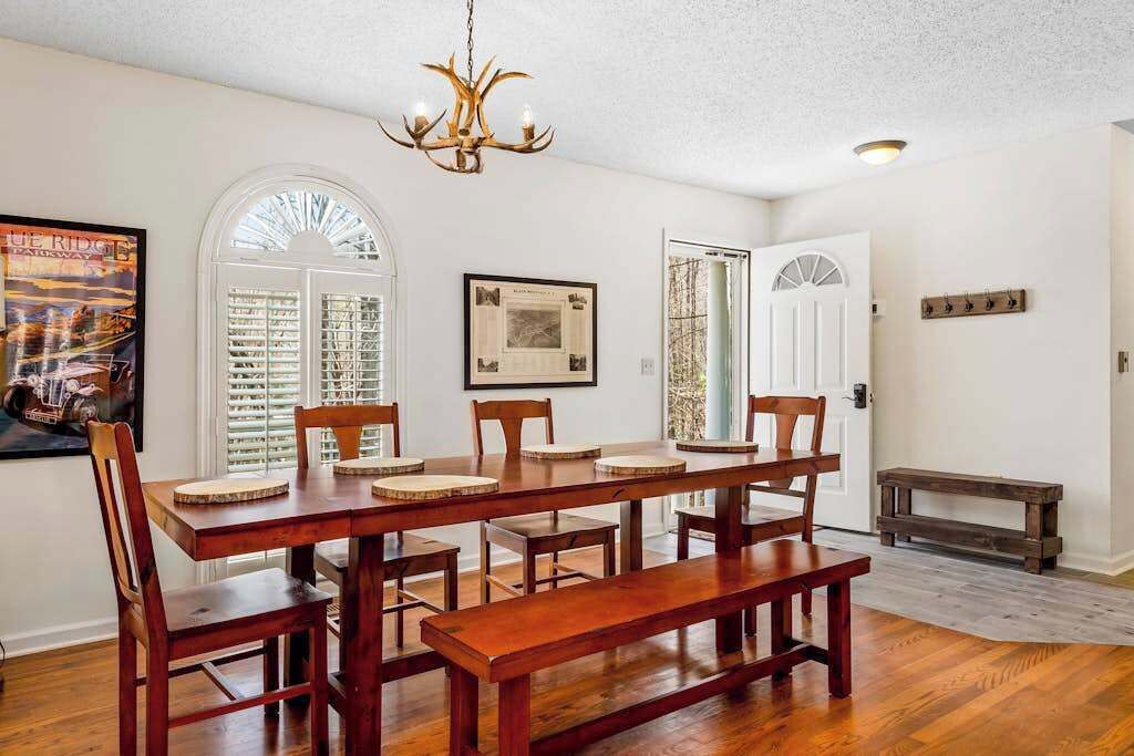 Un comedor con mesa y sillas de madera, una araña y un banco.