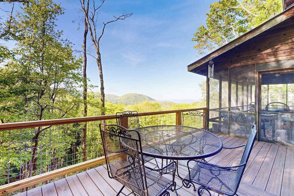 A wooden deck with a metal table and chairs, overlooking a forested area.