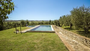 Ein rechteckiger Pool mit Steinrand, umgeben von Rasenflächen und Bäumen.