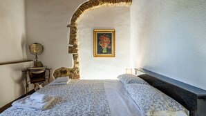 Ein Schlafzimmer mit einem Steinbogen, einem Bett mit floralem Bettzeug, einem gerahmten Gemälde und einem kleinen Tisch mit Spiegel.