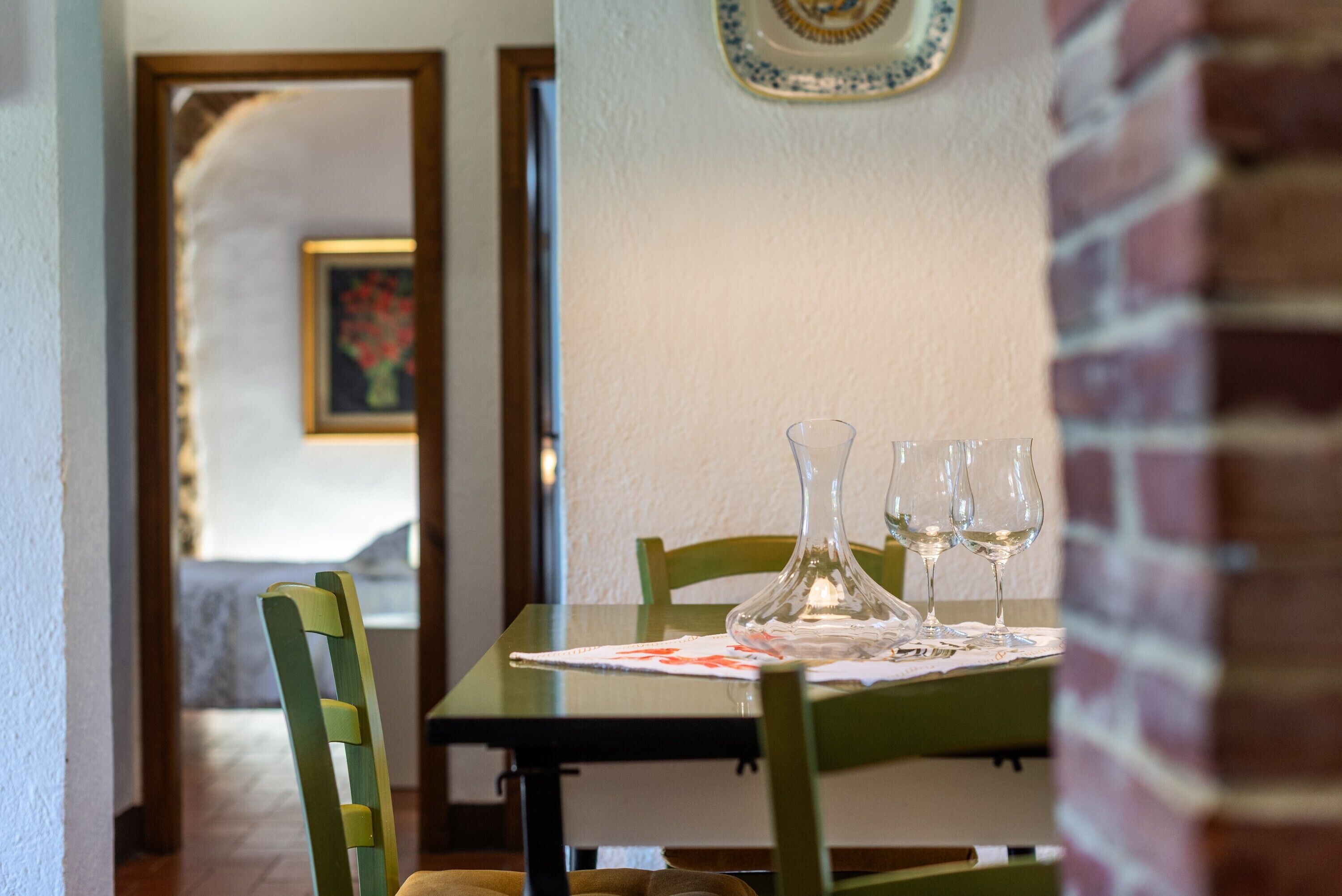 A dining table with two wine glasses and a vase, set against a brick wall with a framed picture.