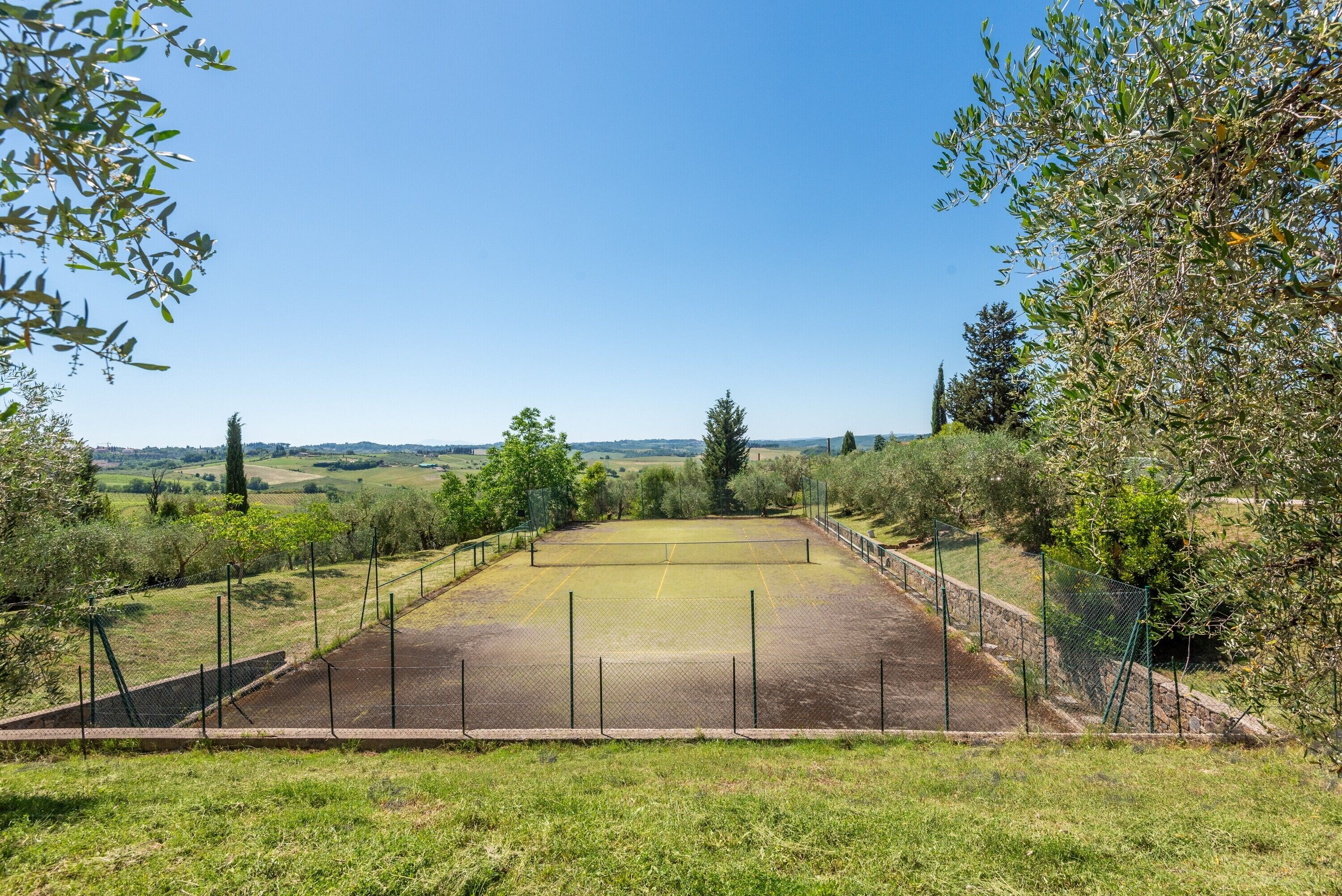 Un court de tennis en plein air, entouré d’arbres, sous un ciel dégagé.