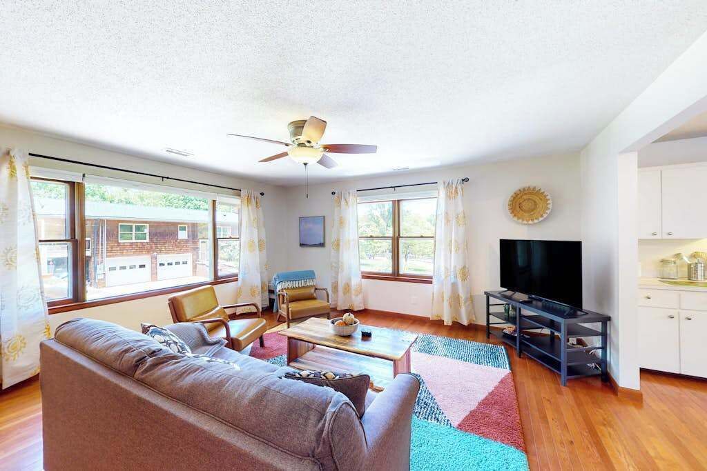 A living room with a sofa, chairs, a TV, and a ceiling fan.