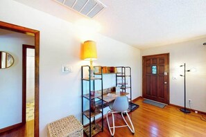 Ein Zimmer mit Holzboden, Schreibtisch mit Lampe, Stuhl, Tür und Spiegel.