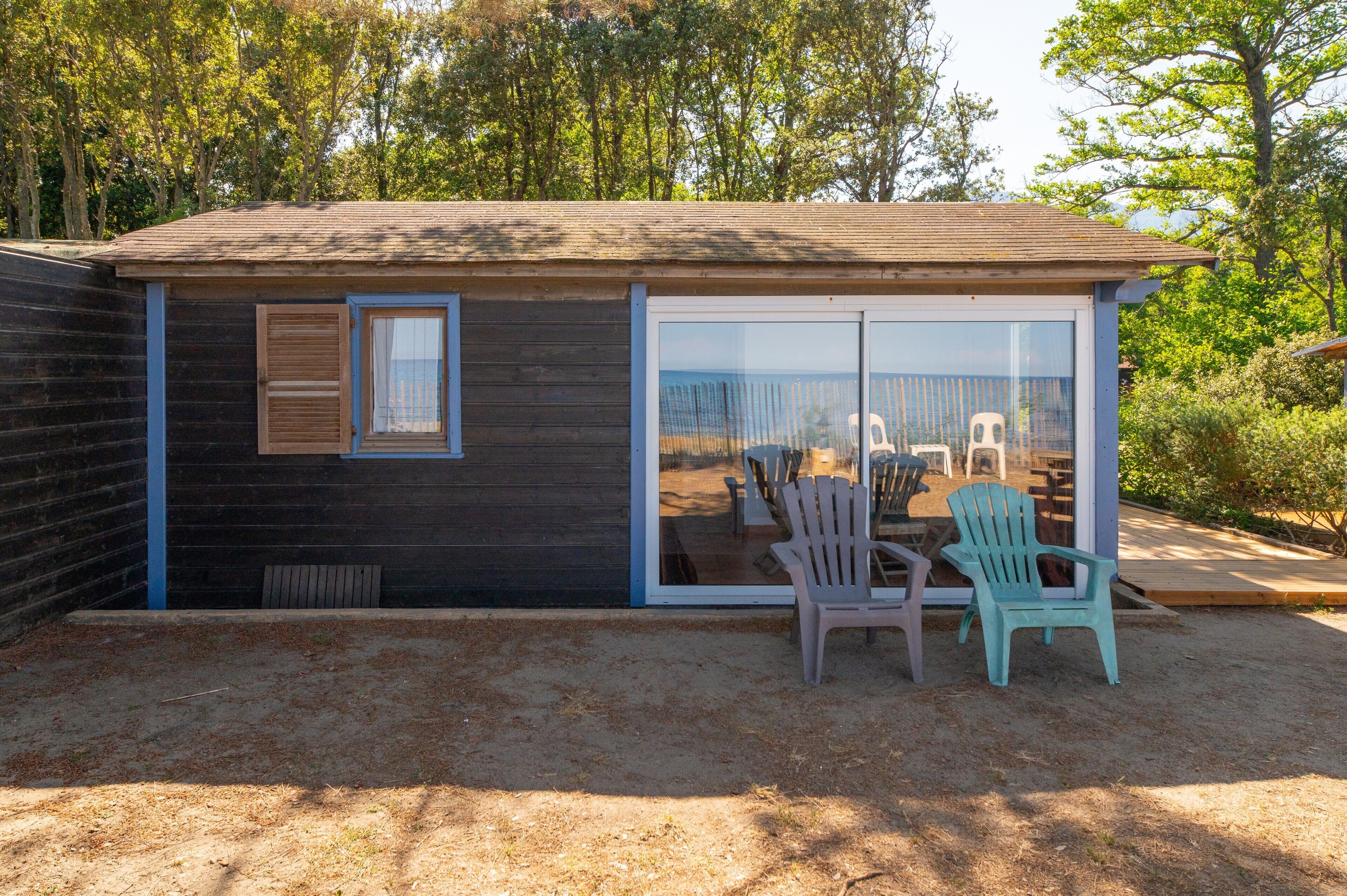 Une petite cabane dotée d’une porte-fenêtre coulissante, d’une fenêtre et d’un espace extérieur aménagé avec des chaises.