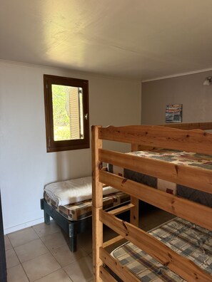 A bunk bed with a mattress and a pillow, a window with blinds, and a wall-mounted light fixture.