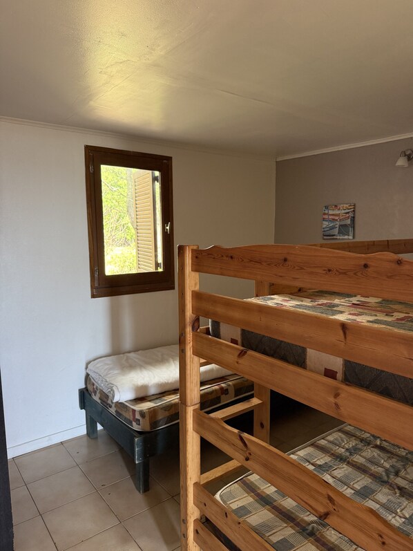 A bunk bed with a mattress and a pillow, a window with blinds, and a wall-mounted light fixture.