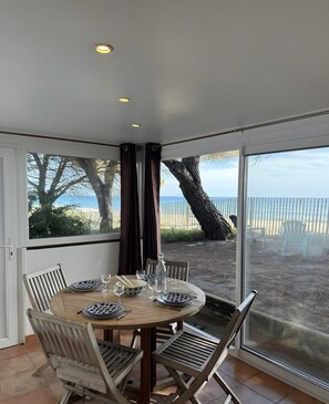 A dining area with a table set for four, large windows with a view of the beach, and a ceiling with recessed lighting.