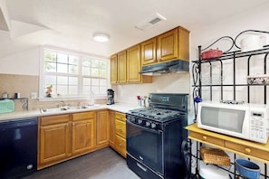 Une cuisine avec des meubles de rangement en bois, une cuisinière, un four à micro-ondes et un lave-vaisselle noir.